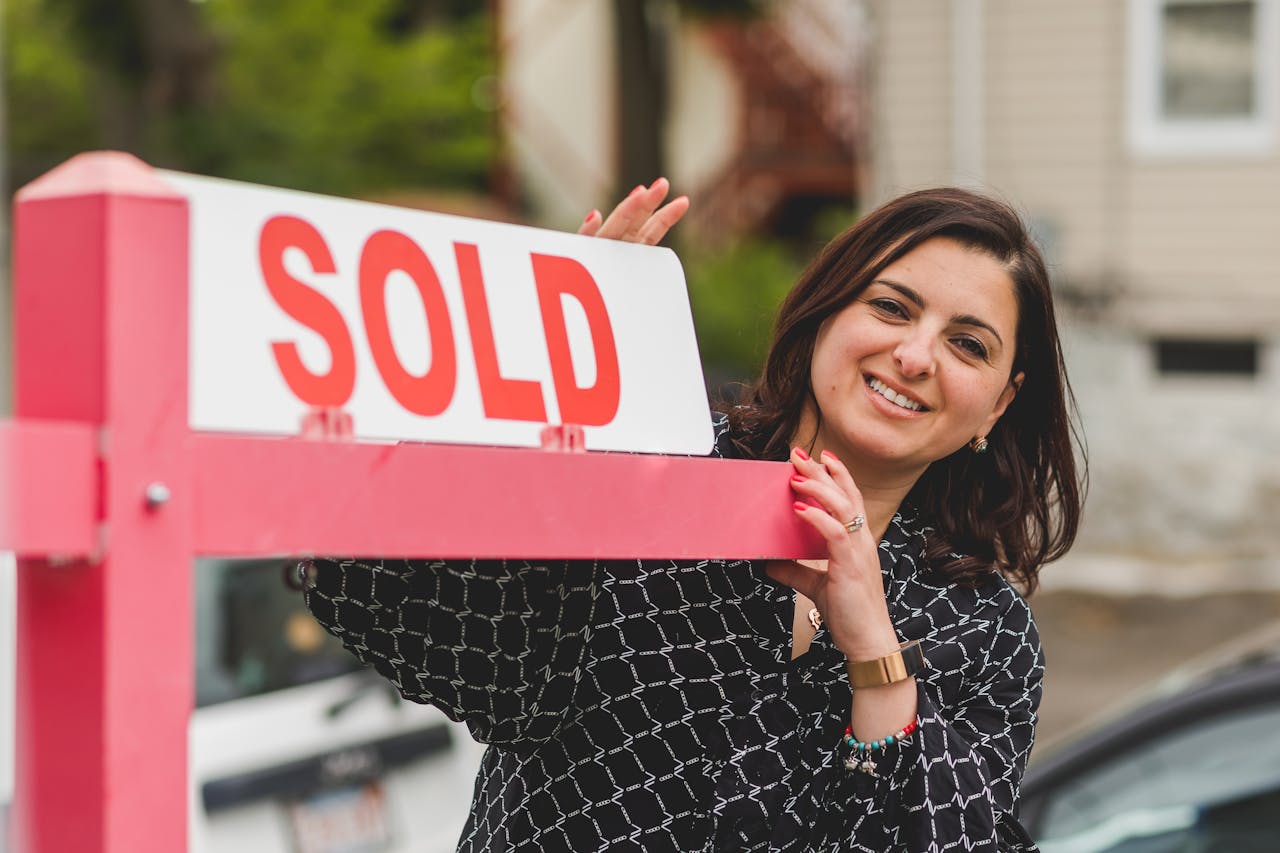 Smiling realtor holding a Sold sign in front of a house. Perfect for real estate marketing.